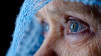 Close up of elderly woman's expressive blue eye with wrinkles and wisdom lines, wearing light blue headscarf in dramatic lighting. Aging concept.