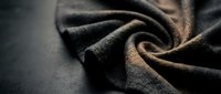 Closeup of dark charcoal wool fabric with soft folds and warm bronze highlights, showcasing natural textile texture and material quality for fashion and design projects.