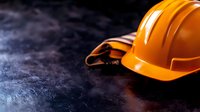 Orange construction hard hat on dark textured concrete background with dramatic lighting and copy space, workplace safety concept for construction industry.
