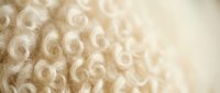Soft cream colored wool yarn texture with curly loops creating cozy knitting material background for craft projects and textile design applications.