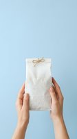 Woman holding blank kraft paper bag with twine bow against blue background for product packaging and branding mockups.
