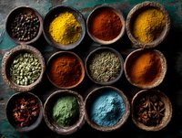 Colorful array of spices and herbs in rustic wooden bowls on dark textured surface, featuring turmeric, paprika, cardamom, and peppercorns for cooking.