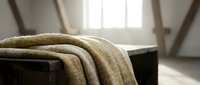 Cozy knitted blanket draped over dark furniture in bright minimalist interior with natural sunlight streaming through window creating warm atmosphere.
