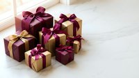 Elegant gift boxes with burgundy ribbons arranged on marble surface near window for holiday celebrations and special occasions.