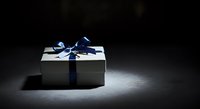 White gift box with blue ribbon bow on dark surface, suitable for holiday, celebration, and luxury product packaging designs.