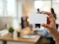Male professional holding blank business card in modern office environment with colleagues in background, suitable for corporate branding and networking concepts.