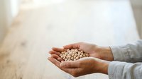 Hands holding white chickpeas or legumes over wooden surface, suitable for food, nutrition, agriculture, and cooking content.