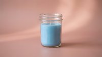 Blue scented candle in glass jar on pink background for aromatherapy relaxation and home decor spa wellness lifestyle.