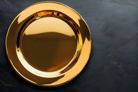 Shiny golden metallic plate on dark textured surface for luxury dining and elegant table setting presentations.
