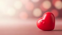 Red glossy heart on soft pink background with warm bokeh lights for Valentine's Day romance love greeting cards wedding invitations romantic designs.