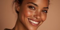 Young mixed-race woman with glowing skin and bright smile showcasing natural beauty and skincare results against warm beige background.