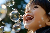 Happy Asian child laughing while playing with soap bubbles outdoors in natural sunlight creating joyful childhood memories and carefree moments.