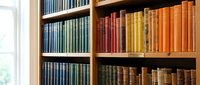 Colorful vintage books arranged on wooden library shelves creating rainbow pattern for educational and literary design projects.