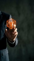 Businessman hand holding glowing orange geometric cube hologram representing innovation, technology solutions and digital transformation concepts.
