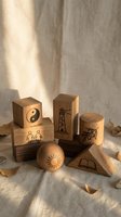 Wooden toy blocks with engraved symbols including yin yang, lighthouse, sun, people, and olive branch on natural linen fabric background with soft sunlight.