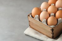 Fresh brown eggs in wooden box on linen napkin against gray background. Natural organic food concept for healthy cooking and baking ingredients.