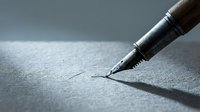 Fountain pen nib writing on textured paper surface, creating fine line strokes for calligraphy, lettering, and artistic writing projects.
