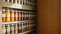 Wooden spice rack with glass jars filled with colorful herbs and spices organized on multiple shelves for kitchen storage and culinary cooking preparation.
