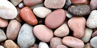 Smooth polished river stones in natural earth tones creating textured background for spa wellness meditation and zen design projects.