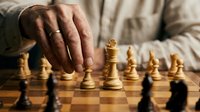Senior man's hand moving wooden chess piece on board during strategic game play session.