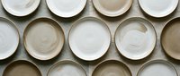 Overhead view of empty ceramic bowls in white and neutral tones arranged in rows, showcasing tableware variety for dining, kitchen design, and culinary content.