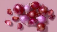 Fresh red and pink shallots with peeled cloves scattered on pink background, top view composition for cooking and food photography styling.