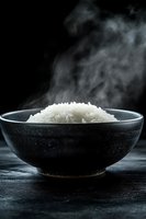 Steaming white rice in black ceramic bowl against dark background, dramatic food photography for restaurant menus and culinary publications.