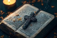 Ornate metal cross necklace resting on open vintage bible pages with glowing candle in dark atmospheric setting, creating spiritual ambiance for religious concept.