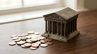 Miniature bank building model with scattered coins on wooden surface representing financial savings and investment concepts for business education.
