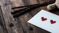 Romantic composition with red hearts drawn on white paper and vanilla pods on rustic wooden background. Soft natural lighting creates cozy atmosphere.