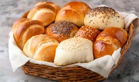 Fresh assorted bread rolls with poppy and sesame seeds in wicker basket lined with white cloth, showcasing variety of golden brown baked goods for bakery or cafe.