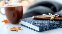 Cozy autumn composition with hot cocoa in brown ceramic mug, knitted scarf, cinnamon sticks and fallen maple leaf against blurred lights background.