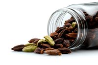 Aromatic cardamom pods spilling from glass jar on white background, mix of green and brown whole spice seeds for cooking and flavoring food.