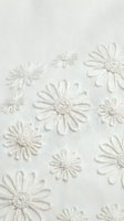 White embroidered daisy flowers on cream linen fabric texture creating elegant floral pattern for fashion design and home decor projects.