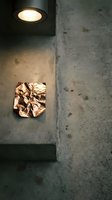 Crumpled gold foil wrapper lies on concrete floor beneath warm recessed lighting, creating dramatic shadows and contrast in minimalist architectural setting.