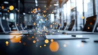 Modern office conference room with glowing bokeh light effects and sparkles floating in air, empty business meeting space with laptops on table, creative atmosphere.