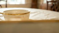 Elegant white porcelain teacup with gold rim on marble table in warm sunlit dining room for luxury hospitality and refined lifestyle concepts.