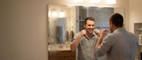 Young Caucasian man brushing teeth in modern bathroom mirror reflection morning routine dental hygiene self-care wellness lifestyle habits.