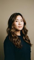 Young Asian woman with long wavy brown hair wearing black sweater against neutral beige background for professional headshot and portrait photography.