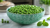 Fresh green peas in decorative turquoise ceramic bowl on marble surface with mint leaves, natural light setting for food photography and healthy eating concept.
