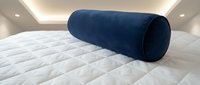 Navy blue cylindrical bolster pillow resting on white quilted mattress under modern ceiling lighting, suitable for bedroom decor and furniture styling.