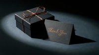 Elegant black gift box with copper ribbon bow and thank you card on dark background, luxury packaging concept.