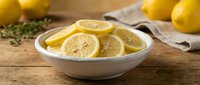 Fresh lemon slices in white bowl on rustic wooden table with herbs and whole lemons, perfect for cooking, beverages and healthy lifestyle concepts.