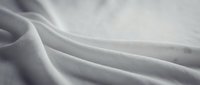 Soft white fabric with elegant flowing folds and gentle curves creating luxurious textile waves for fashion and interior design backgrounds.