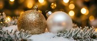 Festive gold and silver ornaments nestled in snow-covered evergreen branches with warm bokeh lights, perfect for holiday marketing and seasonal designs.