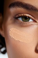 Close-up of green eye with long eyelashes and concealer streak on smooth skin showing makeup application technique for cosmetics and beauty industry use.