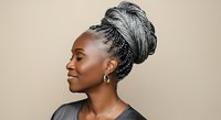 African American woman with braided updo hairstyle wearing silver hoop earrings and black top, shown in profile against neutral beige background for beauty and fashion content.