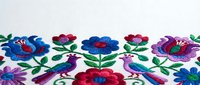 Colorful folk art embroidery with birds and flowers on white fabric. Traditional ethnic needlework pattern featuring vibrant floral motifs and decorative birds.