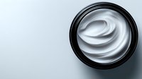 Luxurious white cosmetic cream swirl in black jar photographed from above on light background, showing smooth texture and premium skincare product presentation.