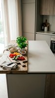 Modern kitchen island with fresh vegetables on cutting board, basil plant and natural lighting creating cozy cooking atmosphere for healthy meal preparation.